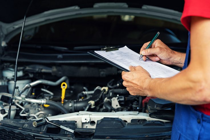 car maintenance and repair mechanic writing checklist paper on clipboard